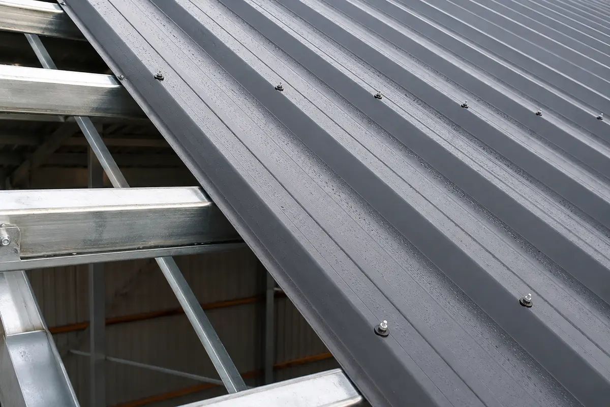 New box-profile steel roof sheeting being fixed to purlins on a farm building