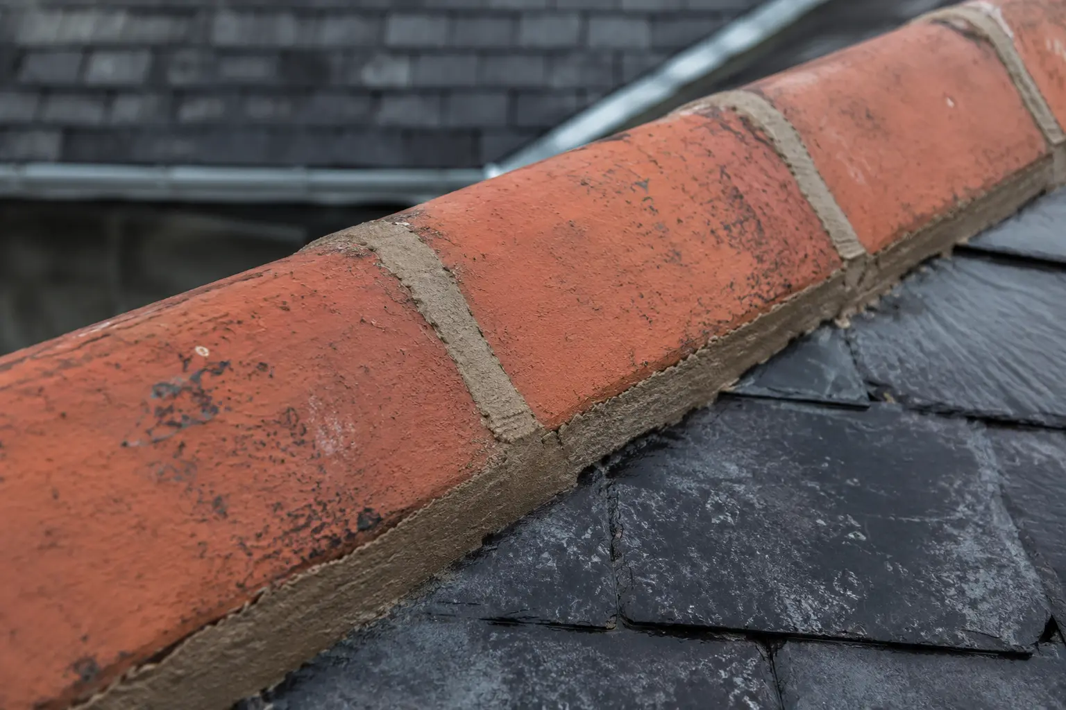 Fresh mortar pointing along a clay ridge tile on a slate roof